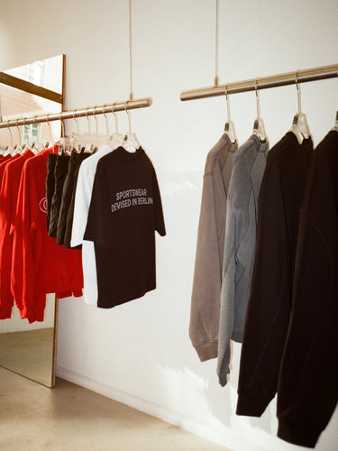 Clothing racks at GRIT pop-up in Munich showcasing red hoodies, black graphic T-shirts, and minimal sweatshirts – curated unisex sportswear collection with Berlin-based design