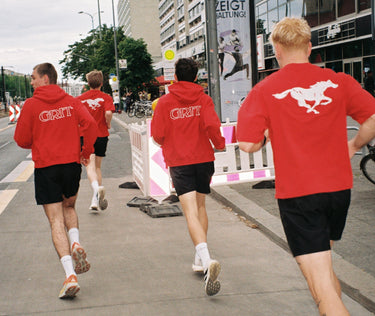 Back view of GRIT team running through the city in coordinated red hoodies and shirts – white GRIT and horse logos on full display, unisex sportswear in action
