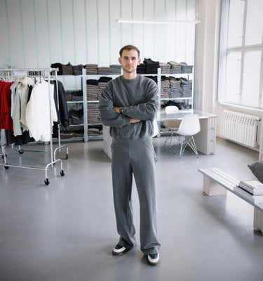 GRIT founder Noah Kolbe in studio wearing full grey tracksuit – standing in front of product shelves and collection racks in brand’s Berlin HQ