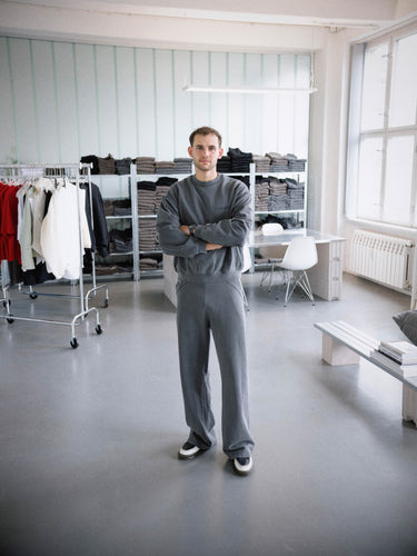 GRIT founder Noah Kolbe in studio wearing full grey tracksuit – standing in front of product shelves and collection racks in brand’s Berlin HQ